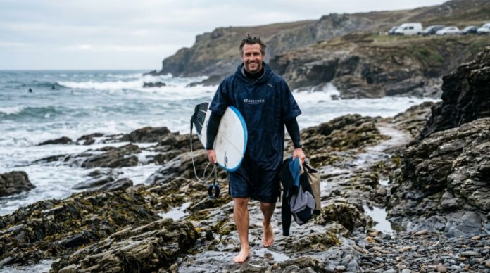 Surfer wearing a high-quality microfibre poncho on a rocky beach after a morning surf session