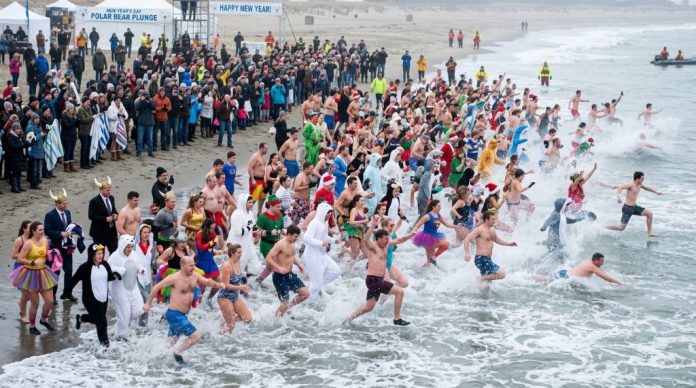 Crowd of participants in costumes running into cold ocean water at a New Year's Day Polar Bear Plunge event